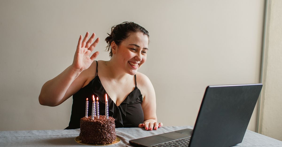 Frau winkt während eines Videochats am Laptop neben einer Geburtstagstorte